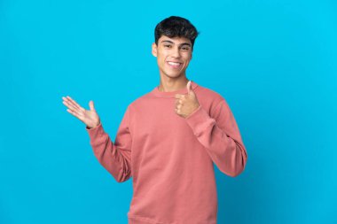 İzole edilmiş mavi arka plan üzerinde genç bir adam. Avucunun içinde hayali bir şey tutuyor. Bir ilan vermek için.