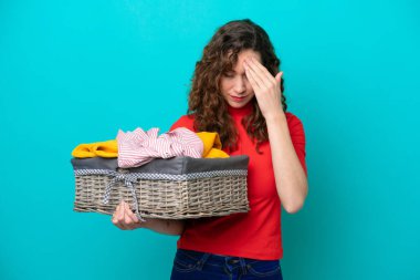 Elinde çamaşır sepeti tutan beyaz bir kadın. Mavi arka planda, yorgun ve hasta bir ifadeyle izole edilmiş.
