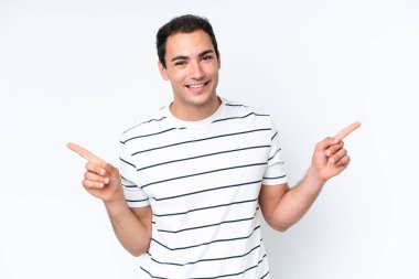 Beyaz arka planda izole edilmiş genç beyaz adam parmak uçlarını işaret ediyor ve mutlu.