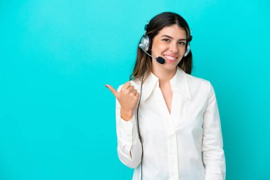 Telemarketer Italian woman working with a headset isolated on blue background pointing to the side to present a product