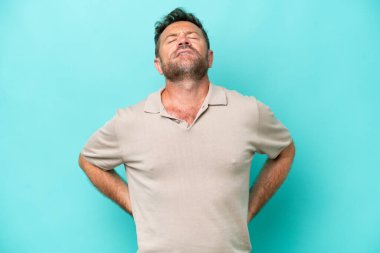 Orta yaşlı, beyaz bir adam mavi arka planda izole edilmiş. Çaba gösterdiği için sırt ağrısı çekiyor.