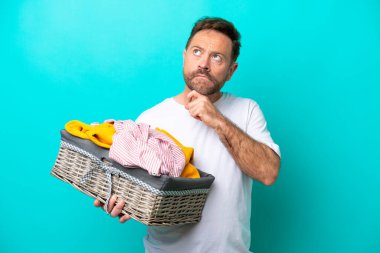 Elinde çamaşır sepeti olan orta yaşlı bir kadın mavi arka planda izole edilmiş bir şekilde yukarı bakıyor.