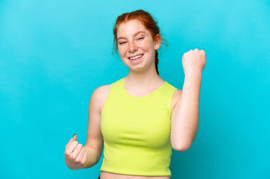 Young reddish woman isolated on blue background celebrating a victory