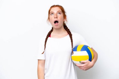 Beyaz arka planda izole bir şekilde voleybol oynayan beyaz tenli genç kadın yukarı bakıyor ve şaşırmış bir ifadeyle