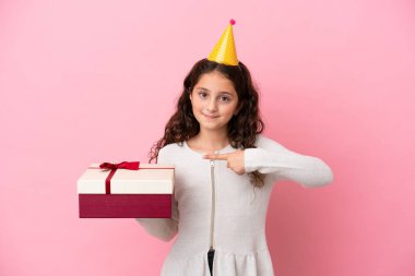 Küçük beyaz kız elinde pembe arka planda izole edilmiş bir hediye tutuyor ve ona doğrultuyor.