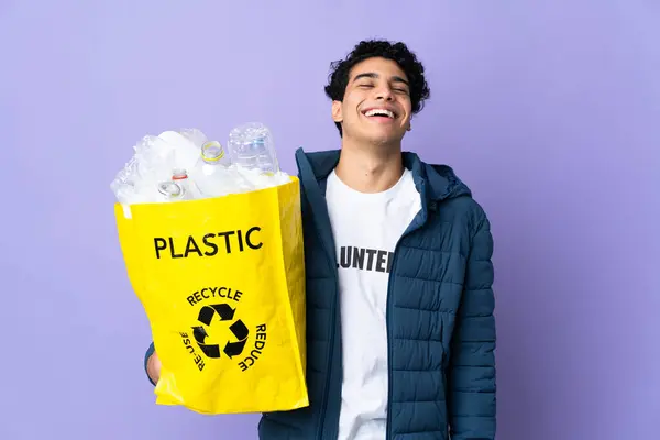 Young Venezuelan man holding a bag full of plastic bottles laughing