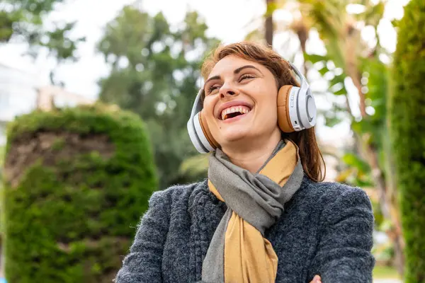 Açık havada müzik dinleyen esmer kadın mutlu ve gülümsüyor.