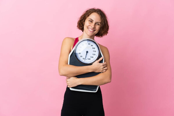 Young English woman isolated on pink background with weighing machine