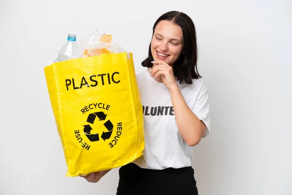 stock image Young caucasian woman holding a bag full of plastic bottles to recycle isolated on white background looking to the side and smiling