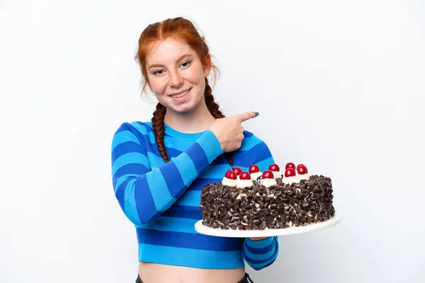 Młoda Rudawa Kobieta Trzyma Tort Urodzinowy Odizolowany Białym Tle Wskazując — Zdjęcie stockowe
