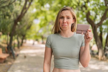 Dışarıda cüzdanını tutan genç sarışın kadın üzgün bir ifadeyle.