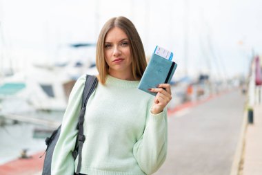 Genç, güzel, sarışın bir kadın elinde pasaport tutarken üzgün bir ifadeyle.