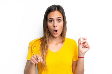 Beyaz arka planda izole edilmiş görünmez diş telleri tutan beyaz kadın şaşırmış ve ön tarafı işaret ediyor.