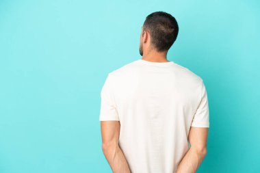 Genç yakışıklı beyaz adam mavi arka planda izole edilmiş ve arkasına bakıyor.