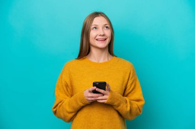 Genç Rus kadın mavi arka planda cep telefonu kullanarak izole edilmiş ve