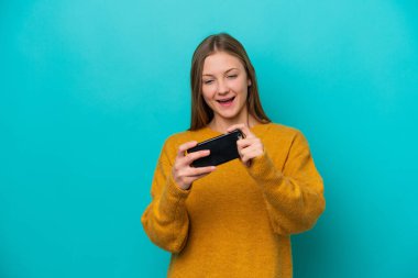 Mavi arka planda izole edilmiş genç Rus kadın cep telefonuyla oynuyor.