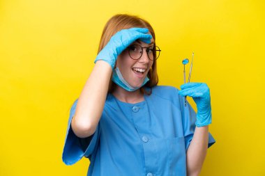 Genç kızıl saçlı dişçi kadın sarı arka planda izole edilmiş. Yan tarafa bakarken sürpriz jest yapıyor.