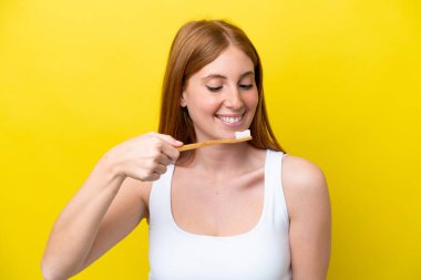 Genç kızıl saçlı kadın sarı arka planda izole edilmiş diş fırçası ve mutlu bir ifadeyle.