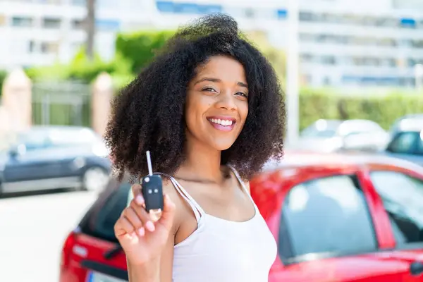 Young African American woman holding car keys at outdoors smiling a lot