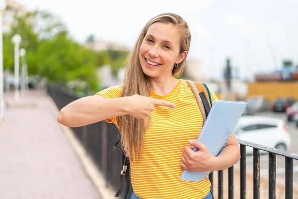 Young Blonde Student Woman Outdoors Pointing — Stock Photo, Image