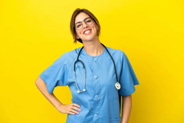 Surgeon doctor woman isolated on yellow background posing with arms at hip and smiling