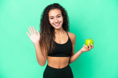 Yeşil arka planda izole edilmiş bir elmayla genç bir Arap kadın mutlu bir ifadeyle selamlıyor.