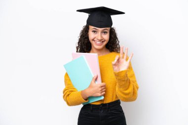 Arap üniversitesinden mezun bir kadın beyaz arka planda kitap tutuyor mutlu ve parmaklarıyla üçe kadar sayıyor.