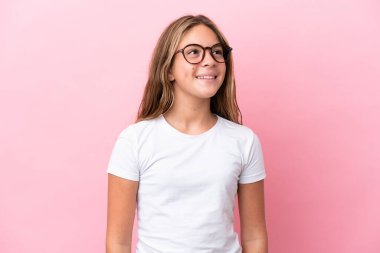 Küçük beyaz kız pembe arka planda izole edilmiş mutlu bir ifadeyle gözlüklü.