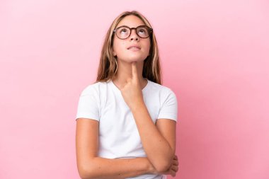 Küçük beyaz kız pembe arka planda izole edilmiş gözlüklü ve yukarı bakıyor.