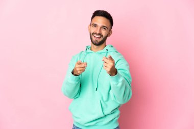 Pembe arka planda izole edilmiş genç beyaz adam şaşırmış ve ön tarafı işaret ediyor.