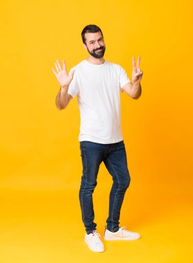 İzole edilmiş sarı arka planda sakallı bir adamın tam boy fotoğrafı. Parmakları olan yedi kişi saydım.