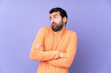 Kafkasyalı yakışıklı adam mor arka planda. Omuzlarını kaldırırken şüpheyle hareket ediyor.