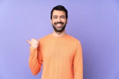 İzole edilmiş mor arka planda beyaz yakışıklı bir adam bir ürünü sunmak için yan tarafı işaret ediyor.