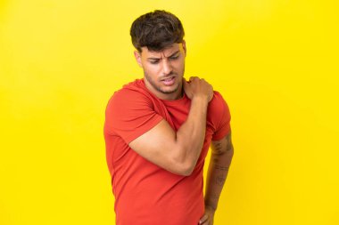 Beyaz tenli yakışıklı, sarı arka planda izole edilmiş, omuz ağrısından muzdarip, çaba sarf ettiği için.