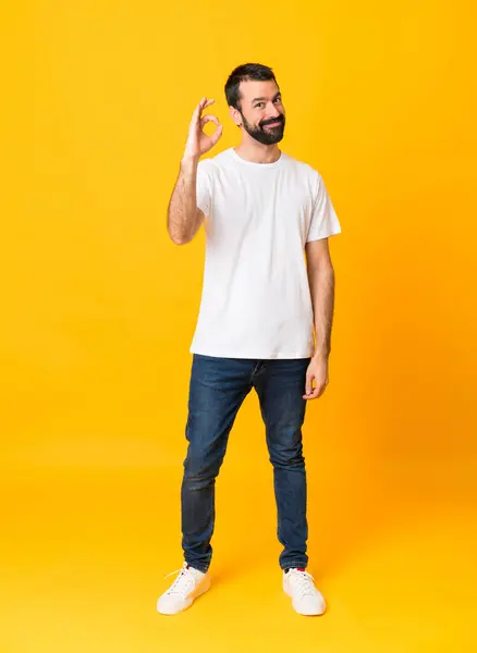 指でOkサインを示す孤立した黄色の背景にひげを持つ男の全長ショット — ストック写真