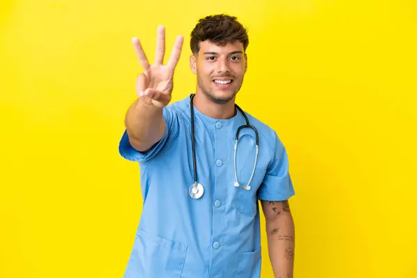 若い外科医の男性は黄色い背景で孤立し 幸せで3つを指で数えました — ストック写真