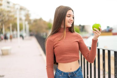 Teenager girl with an apple at outdoors with happy expression clipart