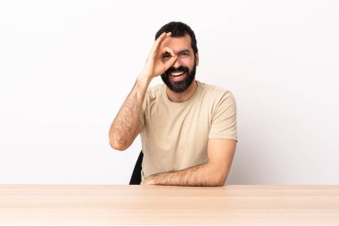 Masada sakallı, beyaz bir adam. Parmaklarıyla 
