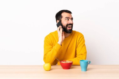Masada kahvaltı yapan beyaz bir adam cep telefonuyla sohbet ediyor..