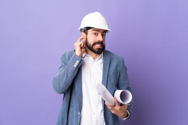 Miğferli genç bir mimar, izole edilmiş mor arka plan üzerinde planlar tutuyor hayal kırıklığına uğramış ve kulaklarını kapatmış.