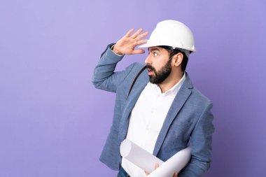 Miğferli genç bir mimar, elinde yalıtılmış mor bir arkaplan, sürpriz bir ifadeyle yan yana bakıyor.