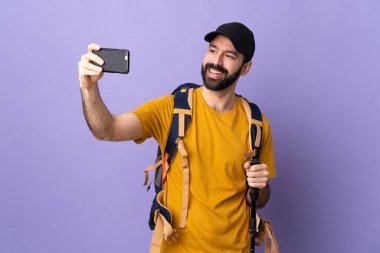 Sırt çantalı ve sırıkla izole edilmiş arka planda yürüyen beyaz yakışıklı bir adam selfie çekiyor.