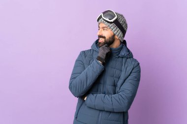 İzole edilmiş mor arka planda snowboard gözlüklü kayakçı yan bakıyor ve gülümsüyor.
