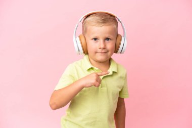 Küçük Rus çocuk pembe arka planda izole edilmiş müzik dinliyor ve gitar hareketi yapıyor.