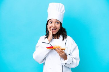 Genç İspanyol aşçı kadın elinde saşimi tutarken mavi arka planda şaşırmış ve şok olmuş bir yüz ifadesi var.