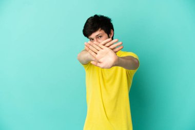 Genç Rus adam mavi arka planda izole edilmiş bir şekilde bir eylemi durdurmak için eliyle jest yapıyor.