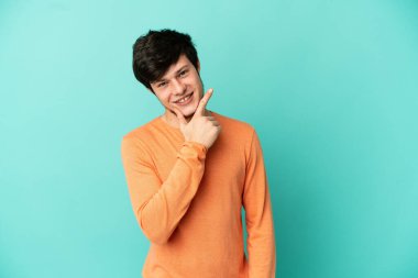 Genç Rus adam mavi arka planda yalnız mutlu ve gülümsüyor.