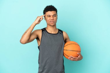 Basketbolcu Afrikalı Amerikalı adam mavi arka planda izole edilmiş. Şüpheleri ve düşünceleri var.