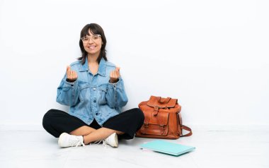 Genç bir kız öğrenci beyaz arka planda tek başına oturmuş para hareketi yapıyor.