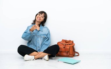 Beyaz arka planda izole bir katta oturan genç bir bayan kendinden emin bir ifadeyle seni işaret ediyor.